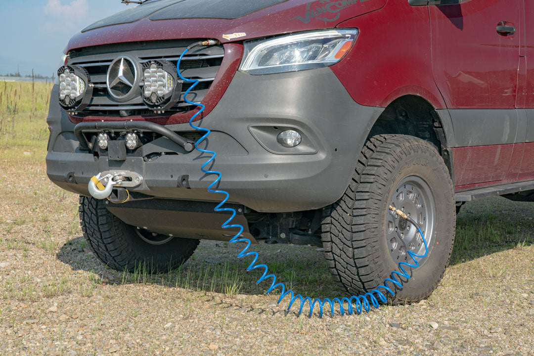 ON BOARD AIR SYSTEM AIRLINE KIT - Sprinter 2019+ by VAN COMPASS, showcasing a red Sprinter van with a blue air hose attached to its tire, highlighting its practicality for off-road adventures.