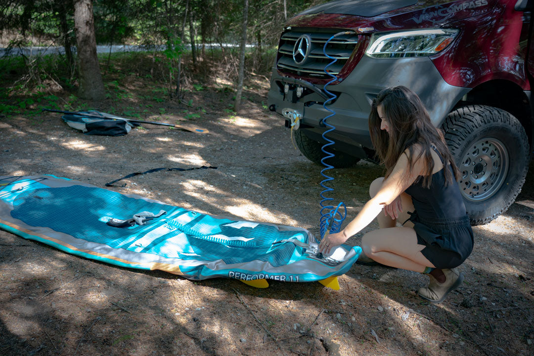 Woman kneeling by a Sprinter van, using a blue air hose to inflate a tire with the ON BOARD AIR SYSTEM AIRLINE KIT - Sprinter 2019+ by VAN COMPASS.
