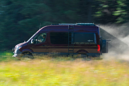 FALCON 3.3 Fast Adjust Inverted Rally Strut by Van Compass for Sprinter 4x4 and AWD, 2015-Present. A van driving through a field, showcasing suspension performance.