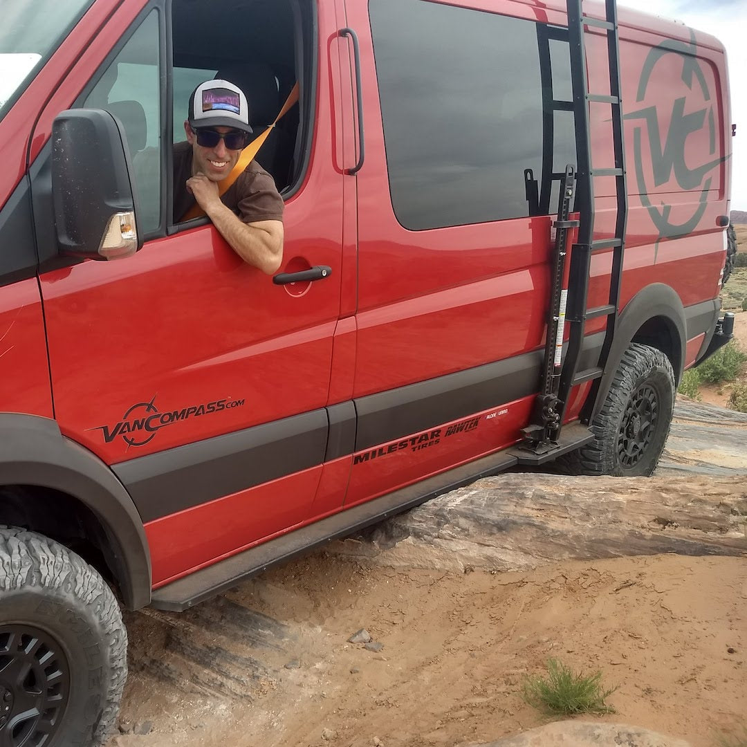 Man in red van showcasing Van Compass Rocker Guards for Sprinter AWD (2023+ 144 wheelbase), featuring sturdy 4 inch steel steps and integrated Hi-Lift jack slots.