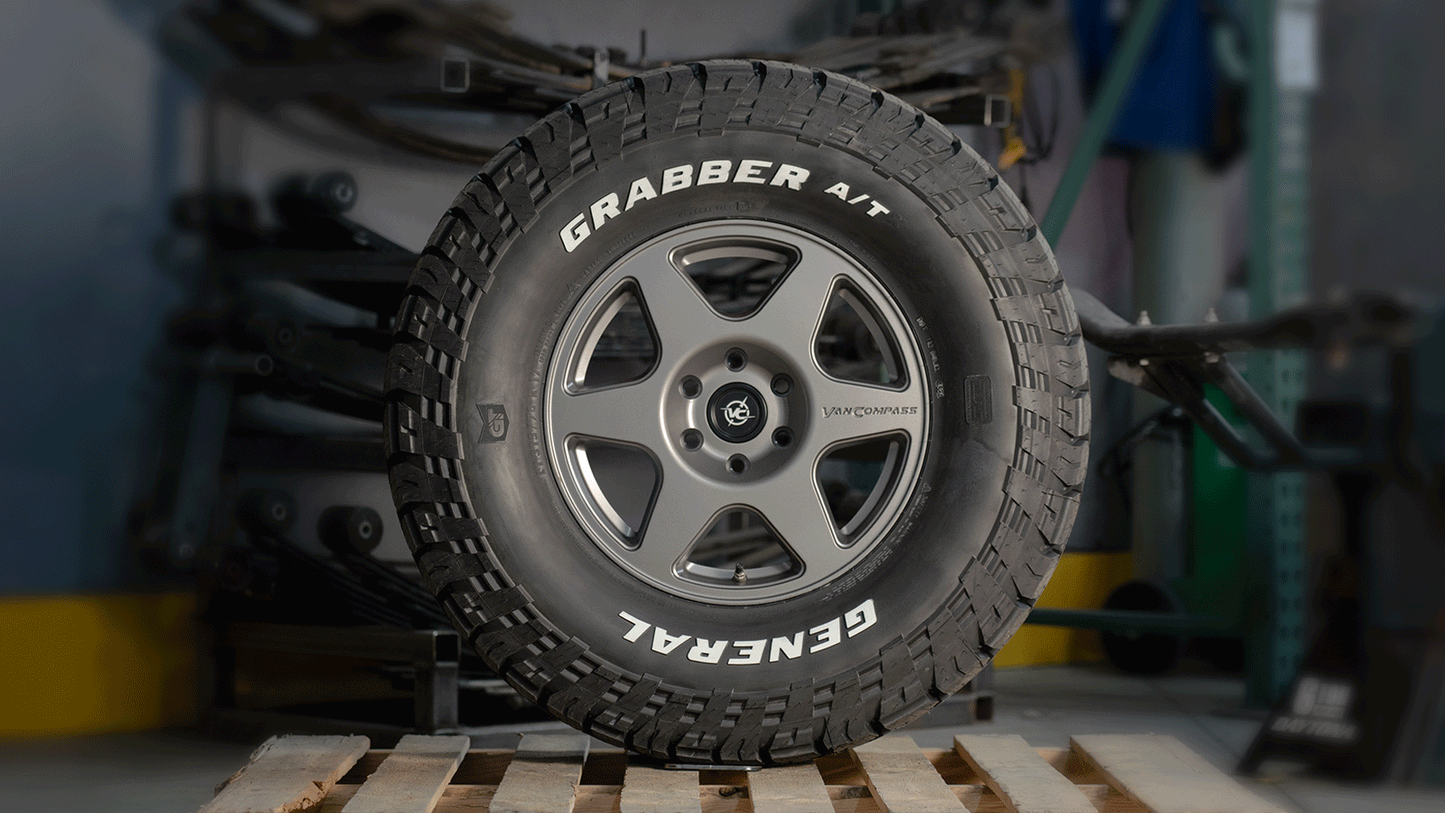 Animated rotating view of the Van Compass SLICE 17” alloy wheel mounted with a General Grabber A/T tire, featuring a sleek, modern five-spoke design and sharp detailing, shown in a workshop setting.