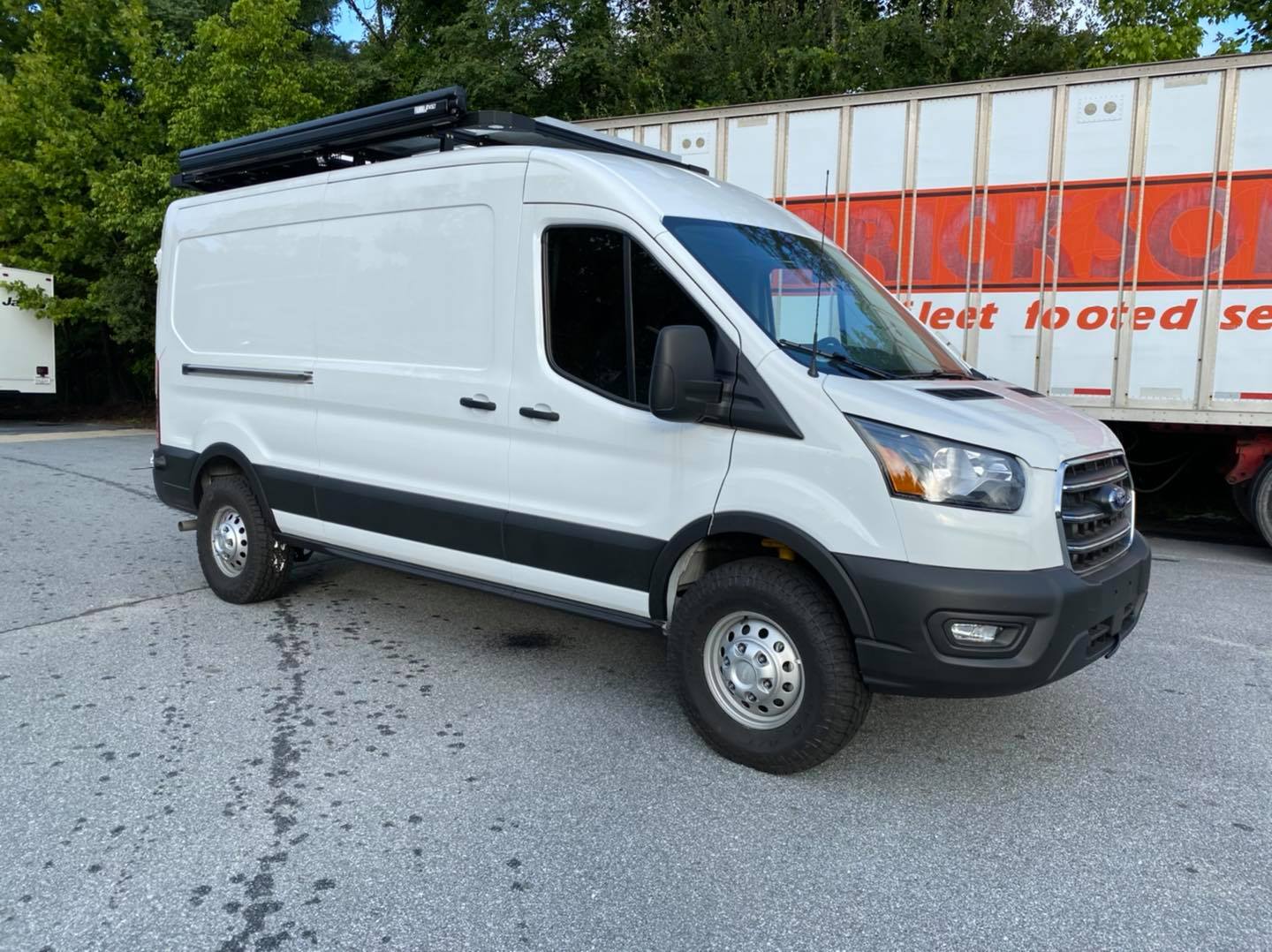 STAGE 2 TOPO 2.0 SYSTEM - TRANSIT RWD (2013+ SINGLE OR DUAL REAR WHEEL), showcasing enhanced suspension components installed on a white van parked in front of a truck.