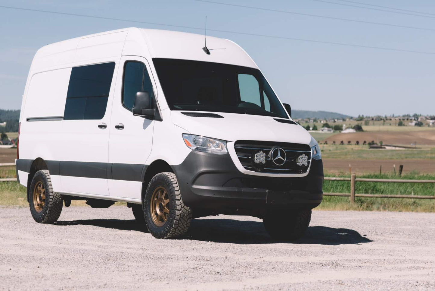 Floating Light Mount for 2019-present Sprinter by Van Compass, installed behind the grille of a parked white van, showcasing aggressive styling and auxiliary light compatibility.