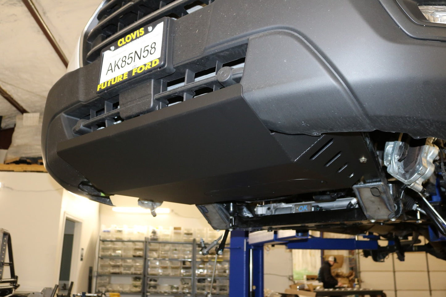 ALUMINUM INTERCOOLER SKID PLATE - TRANSIT (2015+) by VAN COMPASS, shown under the hood of a vehicle, protecting vital engine parts with durable, textured black aluminum construction.