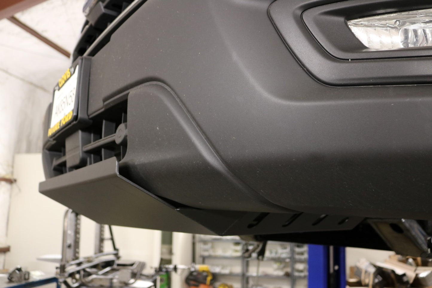 Close-up of the ALUMINUM INTERCOOLER SKID PLATE - TRANSIT (2015+) by VAN COMPASS, showing the robust black-textured finish and protective design for the Ford Transit front bumper.