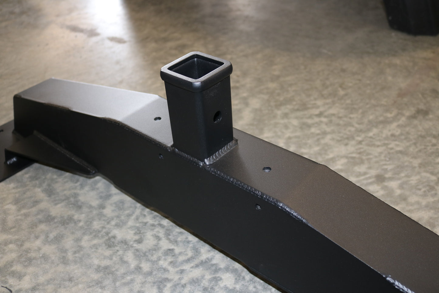 Front Receiver Hitch for Ford Transit (2013+ 1500, 2500, 3500) by Van Compass, showing a black metal piece with a square hole for bike racks or winch.