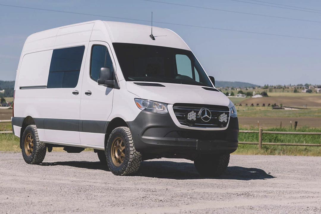 A white van parked on a gravel road, showcasing the Stage 4 System, 2 Lift - Sprinter 2WD (2019+ 2500) by Van Compass, no struts.