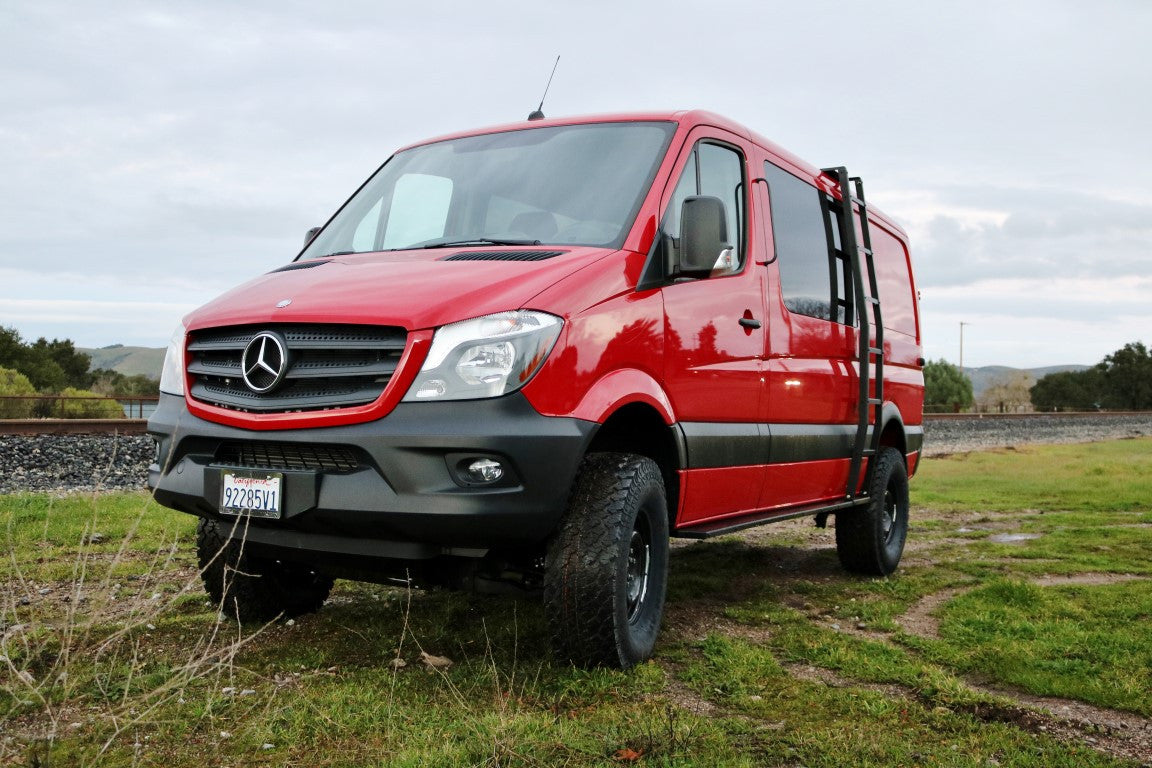 Side view of a red van parked on grass, showcasing the Van Compass Side Ladder for Sprinter (2007-Current, Low Roof Only), attached to the roof ledge.