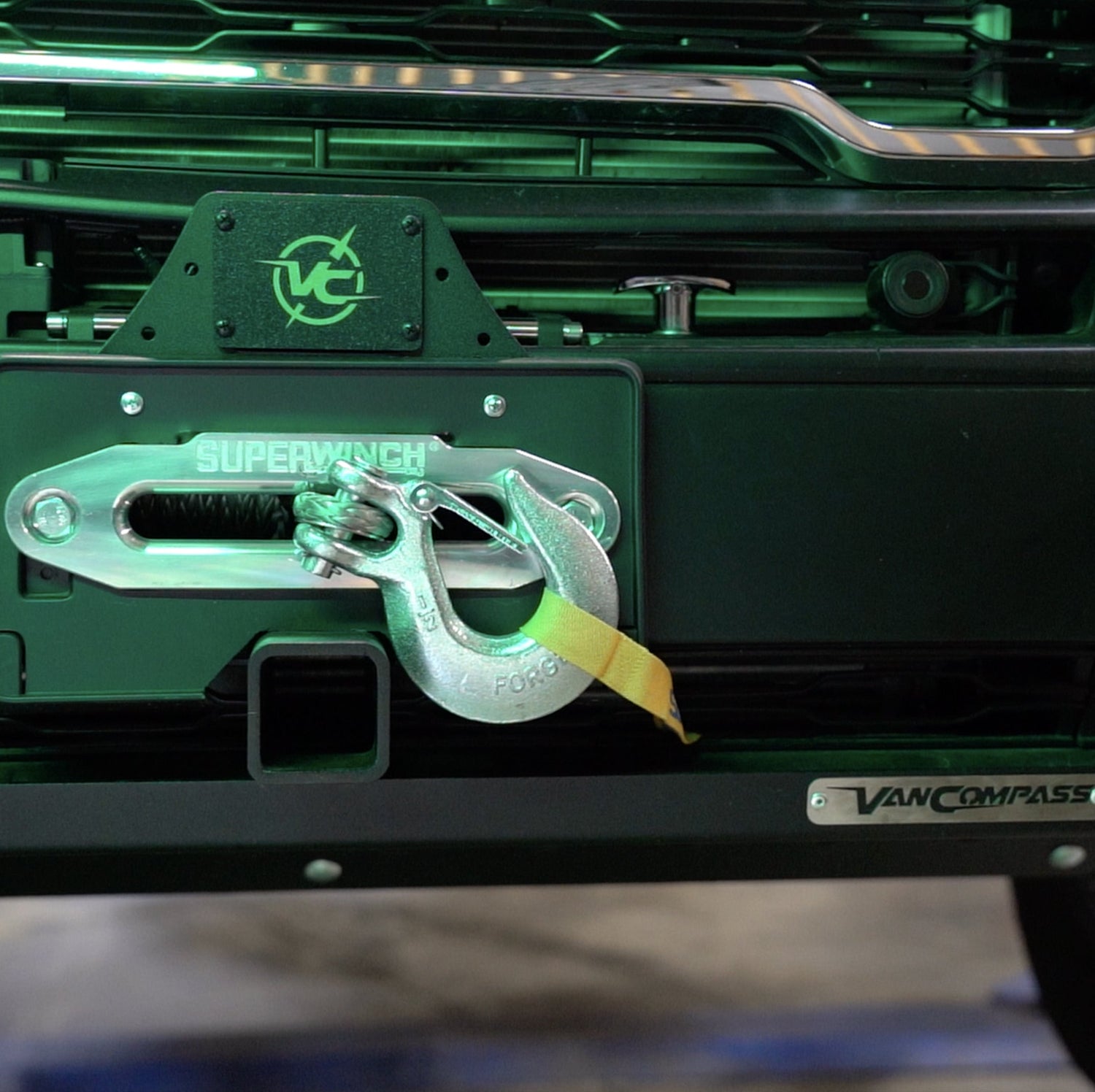 A man standing next to a white van, holding a wire, with the vehicle's headlight and vent visible.
