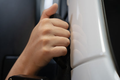 Close-up of a hand gripping an A-Pillar Grab Handle Light Mount on the side of a white 2019+ Sprinter Van, with the reflection of the hand visible on the paint.