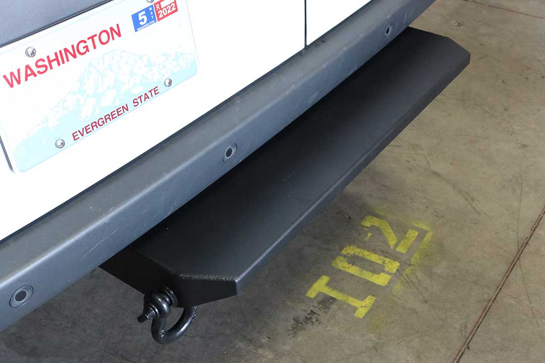 REAR MINI TUG STEP - SPRINTER (2019+) by VAN COMPASS: A black, partial width vehicle step installed on the rear hitch, providing high clearance and extra protection.