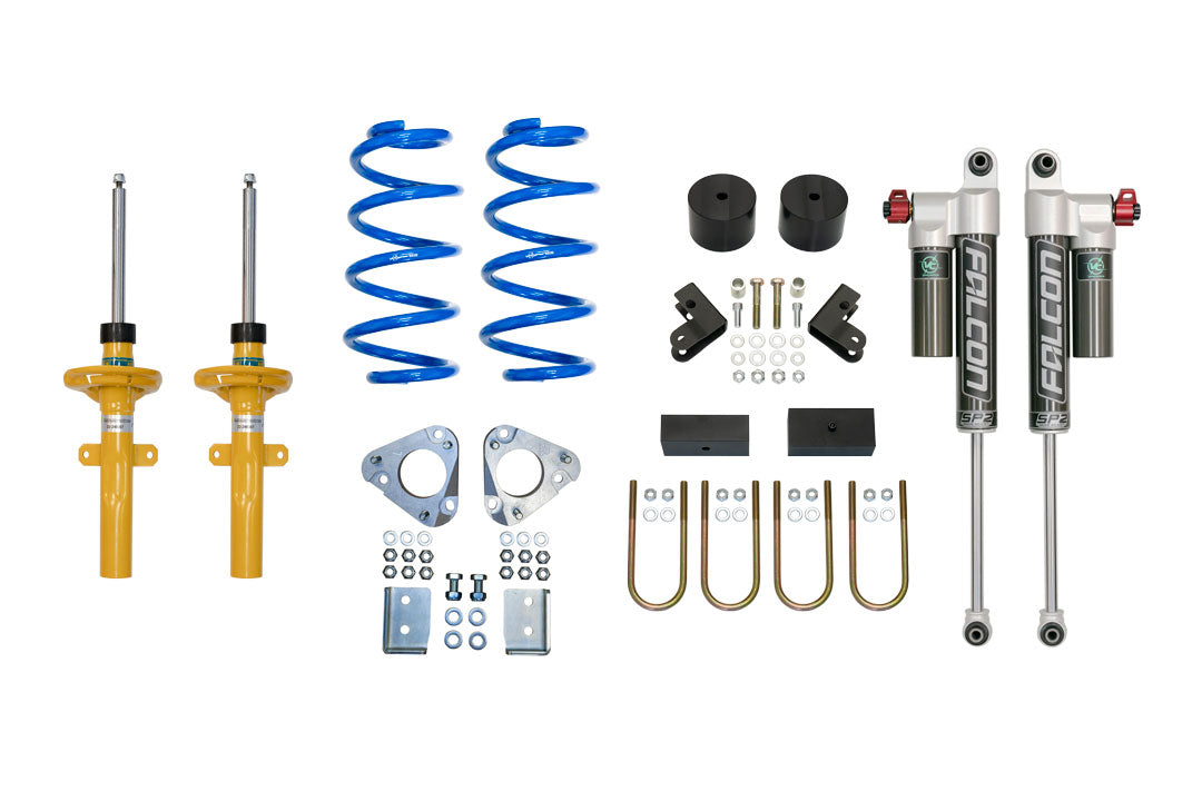 STAGE 2 TOPO 2.0 SYSTEM - TRANSIT RWD (2013+): Vehicle parts set, includes blue springs, yellow cylinder, metal pieces, and adjustable shocks for improved ride quality and handling.