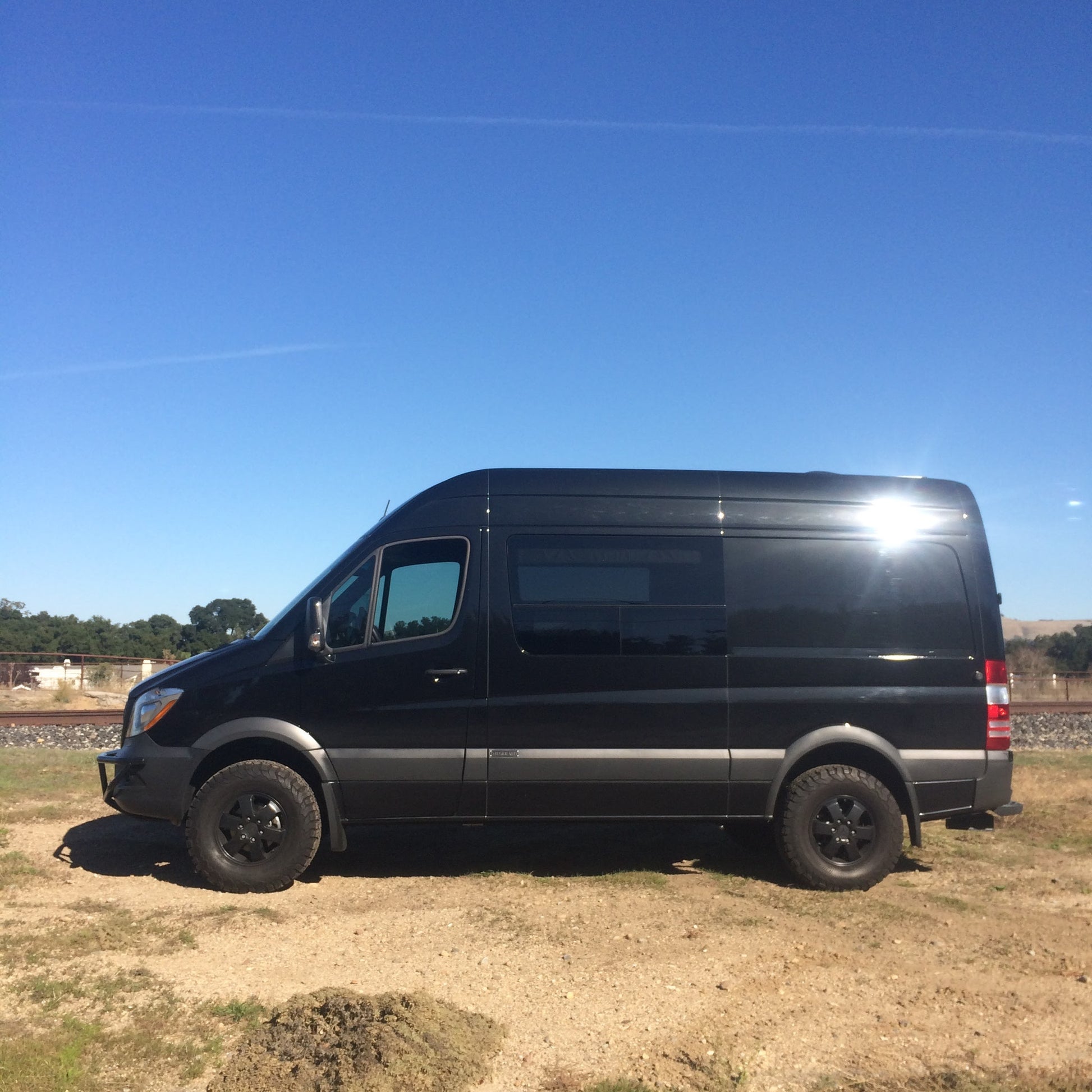 STRIKER 2 Lift Kit (Complete) - Sprinter 2WD (2007-2018) by VAN COMPASS installed on a black van, showcasing enhanced ground clearance and larger tires for off-road capability.