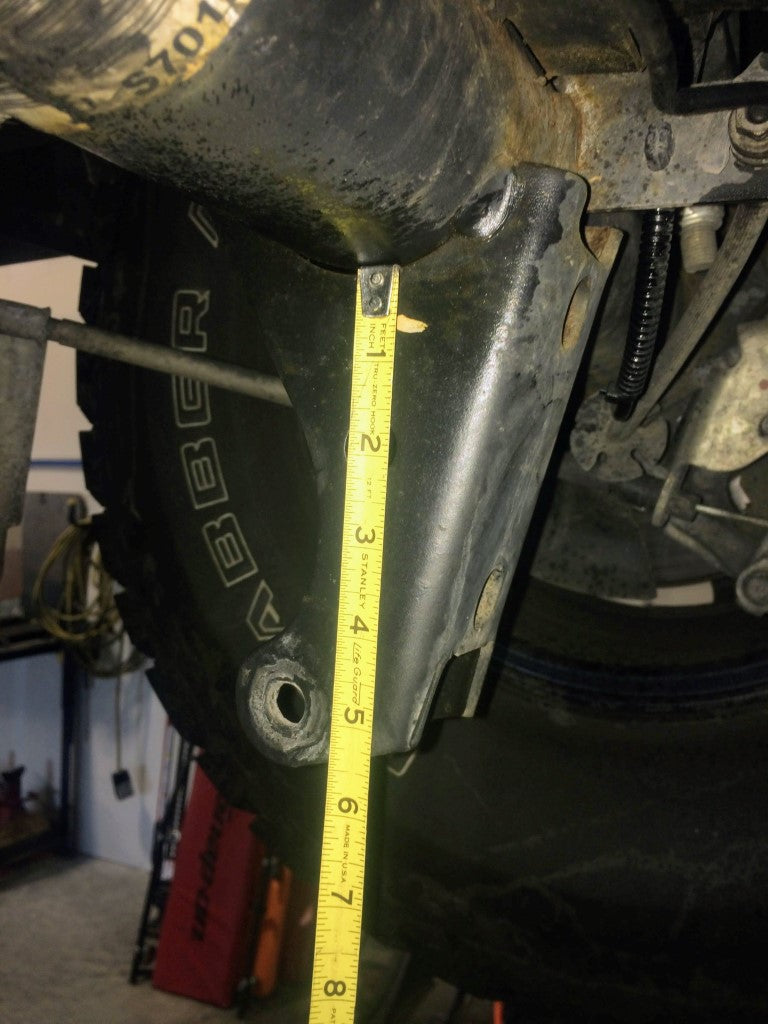 Yellow measuring tape on a vehicle tire, illustrating the REAR HIGH CLEARANCE SHOCK EXTENSION BRACKETS - TRANSIT (2013+) by VAN COMPASS for enhanced ground clearance.