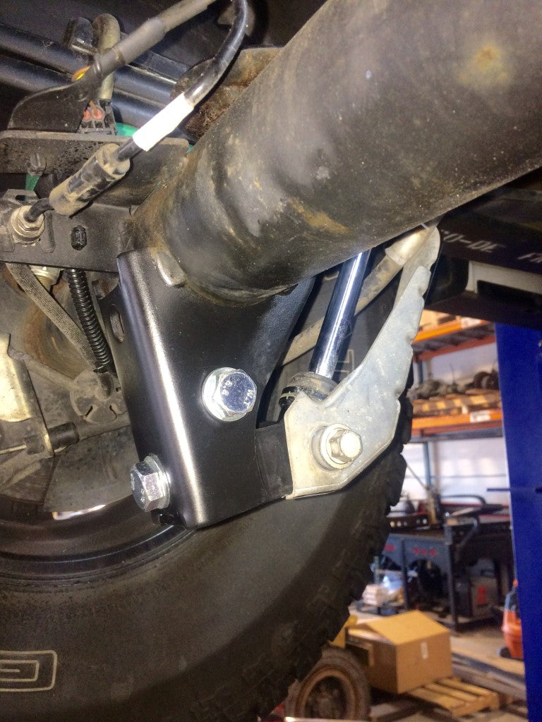 Rear High Clearance Shock Extension Brackets - Transit (2013+) by Van Compass, showing close-up of the metal brackets designed to improve under axle ground clearance and protect shocks.