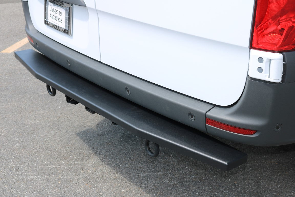 REAR TUG STEP - SPRINTER (2019+) by VAN COMPASS, bolted onto a white Sprinter van's factory rear hitch, enhancing loading ease and protection.