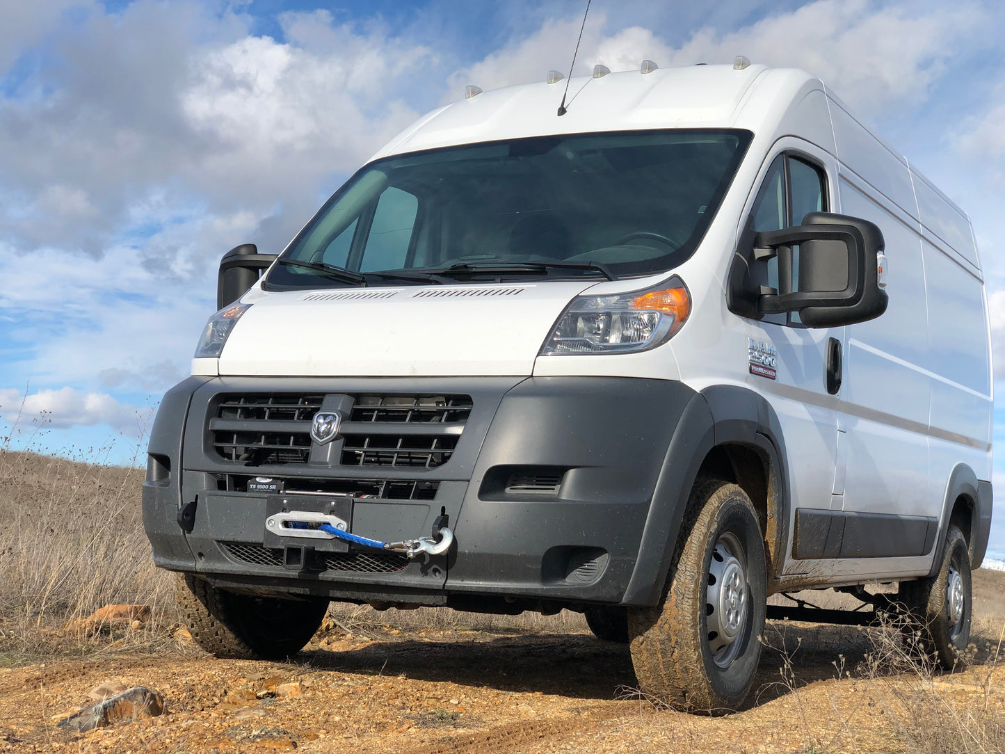 Hidden Winch Mount for 2013-2022 RAM ProMaster by Van Compass, shown installed on a white van parked in a dirt field.