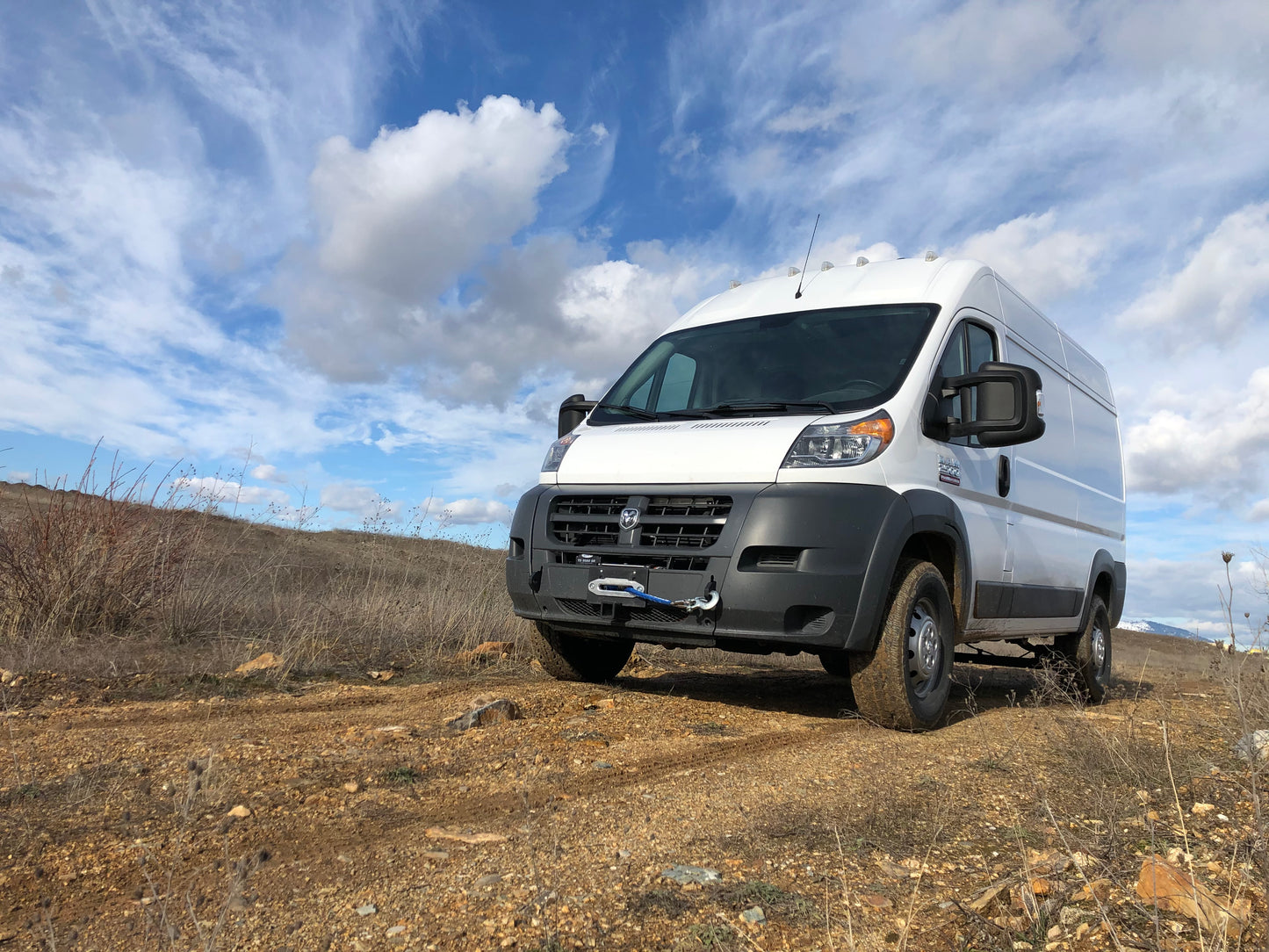 HIDDEN WINCH MOUNT - 2013-2022 RAM PROMASTER by VAN COMPASS, shown on a white van on a dirt road, highlighting its robust front receiver and shackle anchor points.