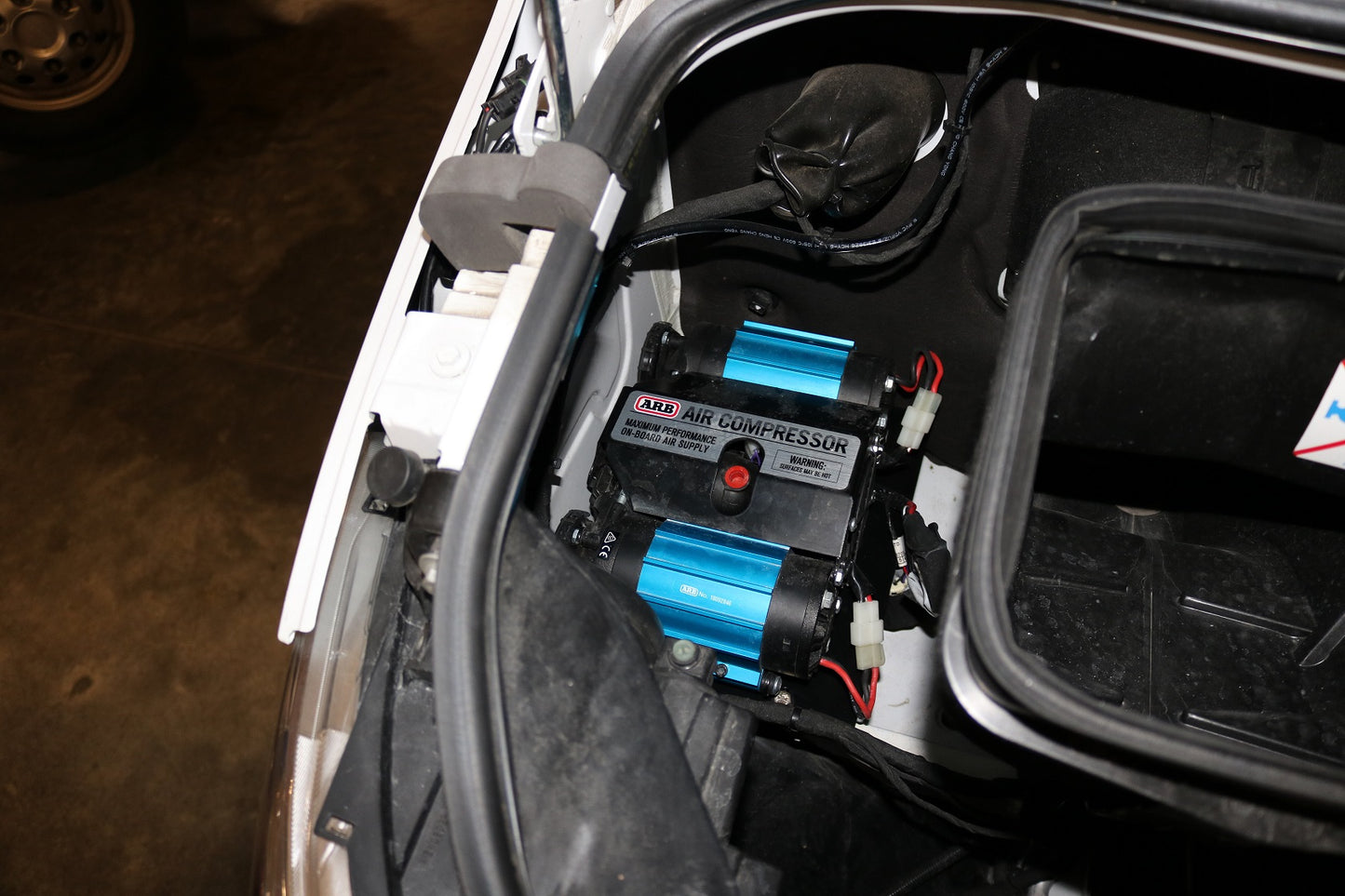 AIR SYSTEM MOUNT - SPRINTER (2019+) by VAN COMPASS shown installed under a car hood, highlighting the blue air compressor and secure mounting near the cabin air filter.